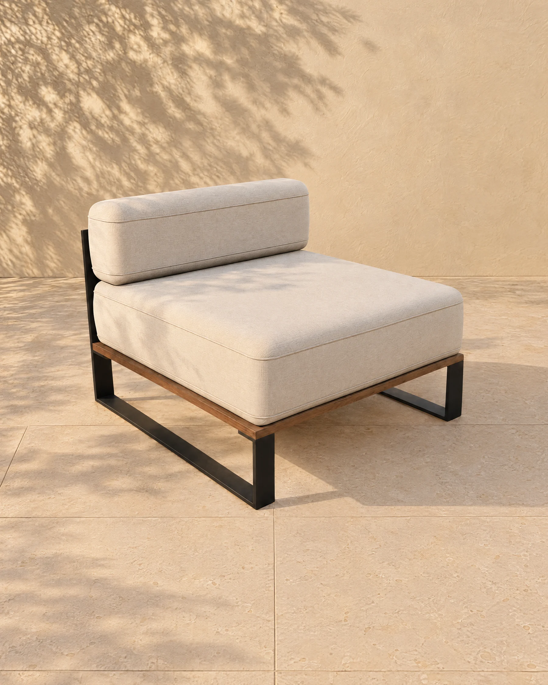 The Nour centre module alone on pale limestone paving before a warm plaster wall: a thin matte black plate sled at each side, a timber deck under a piped seat cushion that stands just proud at the front, and an upright piped back pillow held by two cloth straps round a flat black rail.