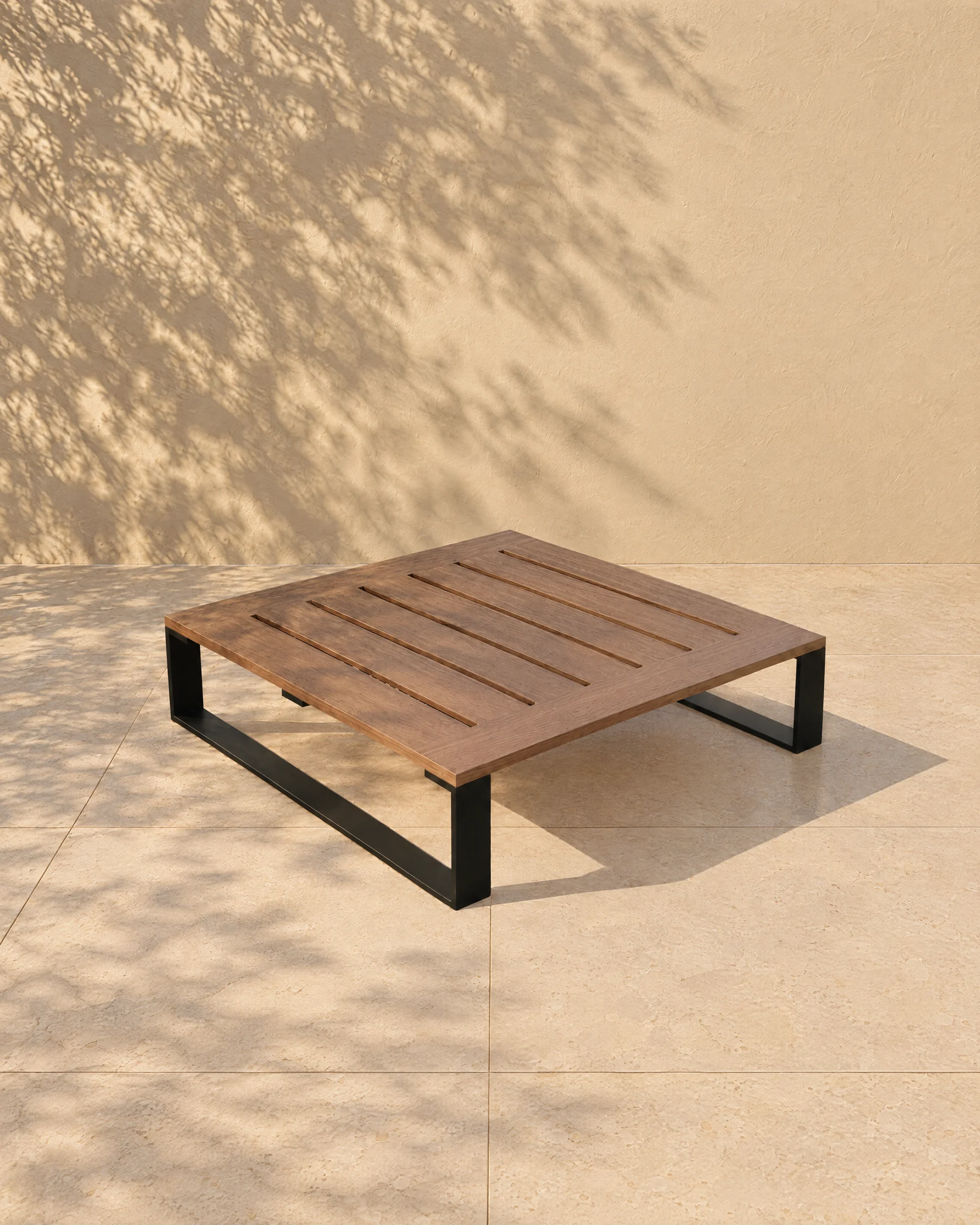 The Nour low table alone on pale limestone paving before a warm plaster wall: the same thin black plate sleds carrying a timber top of seven boards with six slots, 200 millimetres high.